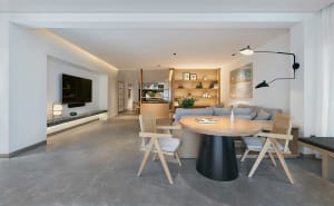 Modern living room with concrete furniture, including a round table with a black base and wooden chairs, a comfortable couch,