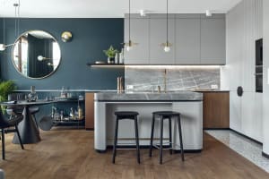Modern residential kitchen with marble countertops and island, grey cabinets, and wooden flooring.