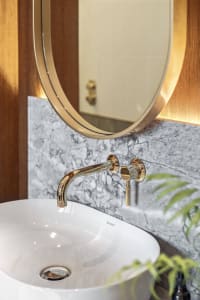 Modern bathroom with marble backsplash, white sink, and gold faucet and mirror.