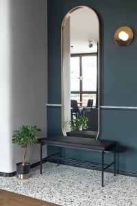 A minimalist entryway features a black metal bench with white marble accents, complemented by a sleek, oval-shaped mirror wit