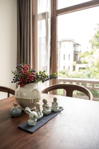 A wooden table with a ceramic vase filled with berries and small ceramic figures on a blue mat, set against a backdrop window
