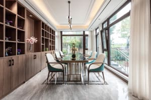 Modern dining room featuring a marble table with glass base and wooden chairs, surrounded by bookshelves filled with decorati