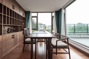 Interior of a modern home office with wooden furniture and large windows overlooking greenery.