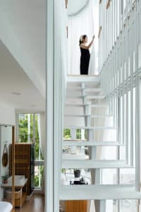 A modern white staircase made of glass with a minimalist design, featuring a woman standing near the railing.