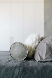 A minimalist bedroom with grey pillows and a plush white furry blanket on a bed with dark grey bedding.