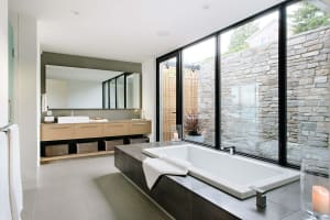 Modern bathroom featuring wood vanity, stone walls, and concrete bathtub