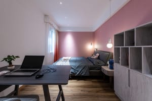 A minimalist bedroom featuring neutral-colored furniture and a pink accent wall.