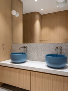 Modern bathroom with blue sinks, wooden cabinets, and textured backsplash.