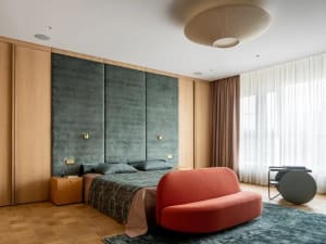 Modern bedroom featuring a wooden headboard and upholstered seating area with a plush red bench and a large window with white