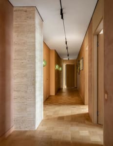 A modern, minimalist corridor with wooden flooring, green spherical lights, and framed artwork.