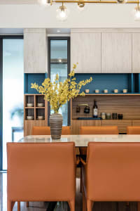 A modern dining room featuring wooden furniture and glass elements, with a vase of yellow flowers on the table.