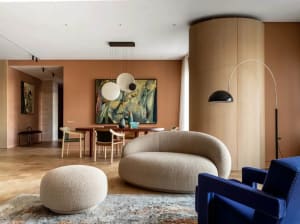 A modern living space featuring a white circular sofa, white footstool, and wooden flooring.