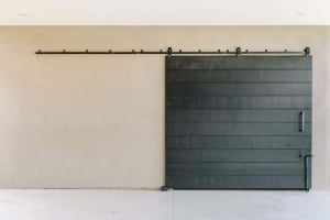 A modern, minimalist barn door wall featuring a horizontal black slat wall on a beige wall with a black metal rail mounted ab