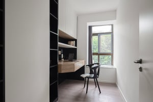 A minimalist home office featuring a wooden desk and glass window, with a black chair and open book.