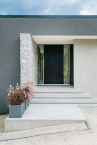 A modern residential entrance featuring a black door, concrete steps, and stone accents.