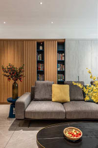 Modern minimalist living room featuring a gray sofa with yellow throw pillows, a black marble coffee table, and a wooden book