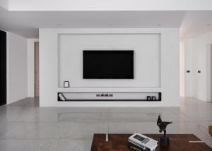 A modern living room with minimalist design featuring smooth concrete walls and floor, a large flat-screen TV mounted on the 