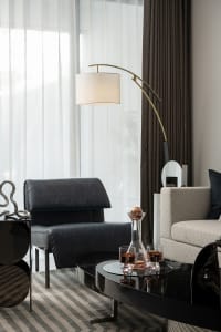 A modern living room with a black leather armchair, a beige sofa, and a round black coffee table with a white lamp, glass dec