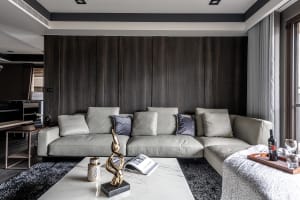 Modern living room with a grey leather sofa, wooden accent wall, and a marble coffee table with decorative items.
