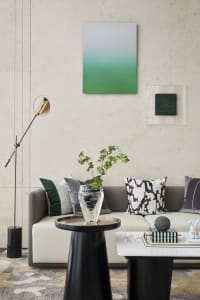 A modern living room featuring a white sofa with green and black pillows, a black side table with a vase and greenery, and a 
