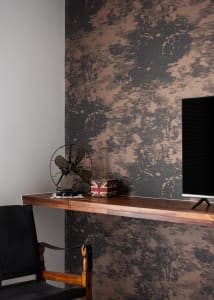 A minimalist office space featuring a metallic desk with a vintage fan and a trunk on top, against a metallic-patterned wall.