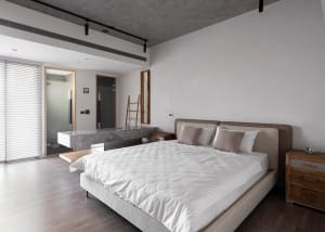 A minimalist bedroom featuring a bed with a concrete headboard and wooden furniture, in a modern industrial style.