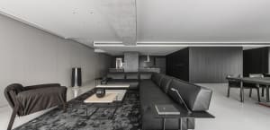 Modern living room with a black leather sectional sofa, concrete floor, and minimalist design