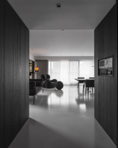 Contemporary living room with minimalist design, featuring a concrete floor, black furniture, and large windows with sheer cu