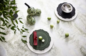 Modern green ceramic dinnerware with red napkins and green apples on a light, textured table surface.