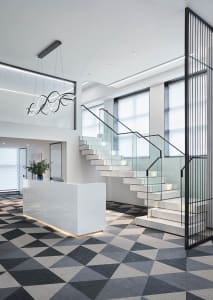 Modern office reception area with marble and glass staircase bordered by black metal railing.