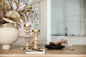 Decorative accessories featuring wooden candle holders with a gold finish and dried plants in a vase.