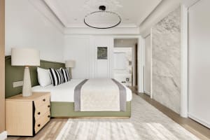A modern bathroom featuring marble flooring, wooden cabinets, and a green upholstered bed.