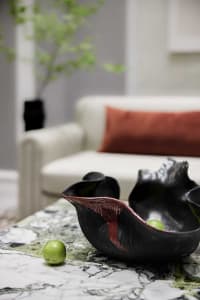 A modern living room with a marble coffee table displaying black ceramic bowls and green spherical ornaments, positioned in f