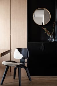 A modern home office features a black cabinet, a cowhide-covered chair, and a round mirror on a dark wall.