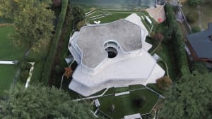 An aerial view of a modern house with a unique shape and concrete exterior.