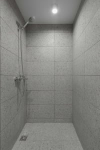 A minimalist shower area with concrete tiles walls and floor, featuring a shower head mounted on the wall and a ceiling light