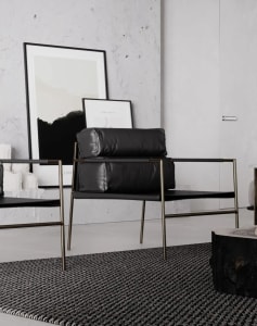 A modern minimalist living room with black leather and gold metal furniture, concrete flooring, and framed pictures on a text