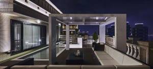 Modern rooftop patio with concrete and glass elements, featuring a lounge area and cityscape view at night.
