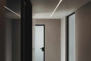A modern corridor featuring concrete walls and floor with linear LED lighting fixtures.