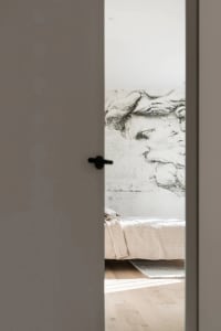 A minimalist bedroom featuring a concrete wall with a large, detailed wall mural of a classical statue's head, a bed with a t