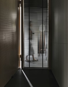 A modern doorway with metal blinds partially open, showing a wooden floor and a person standing behind the blinds.