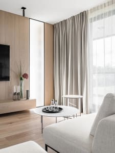 A modern living room with minimalist decor, featuring a sleek sofa, wooden cabinets, and a large window with sheer curtains, 