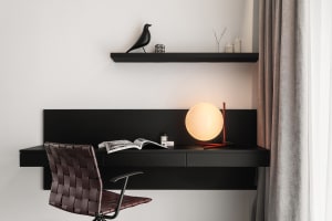 A modern black wood home office setup with a leather chair, minimalist desk, and green plant.