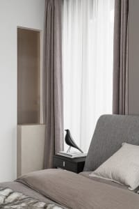 A modern grey bedroom featuring a grey upholstered bed with a bird sculpture on a bedside table.