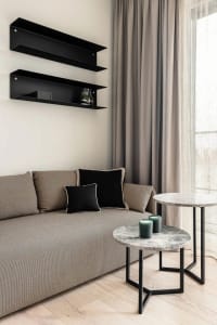 A modern living room featuring a grey couch adorned with black cushions and black floating shelves on the wall.