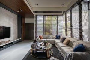 A modern living room featuring a large leather sofa, a glass coffee table, and a flat-screen TV on a marble wall.