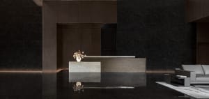 A modern lobby with a concrete reception desk, white vase with flowers, and a grey sofa on a white rug.