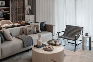 A modern living room with neutral-toned furniture, including a white sofa with patterned pillows, a glass coffee table, and a