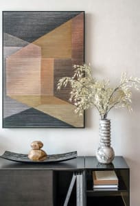 Modern art piece featuring geometric shapes painted with marble tones, displayed on a shelf with a vase and books.