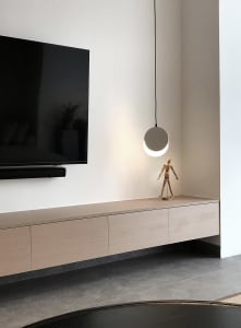 A minimalist living room with a concrete wall, wooden flooring, and floating shelves.